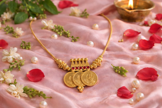 Three Coin Lakshmi Pendant Mala – traditional South Indian temple jewellery with three Lakshmi coin pendants, crown-inspired connector and ruby-tone stones styled on pink satin