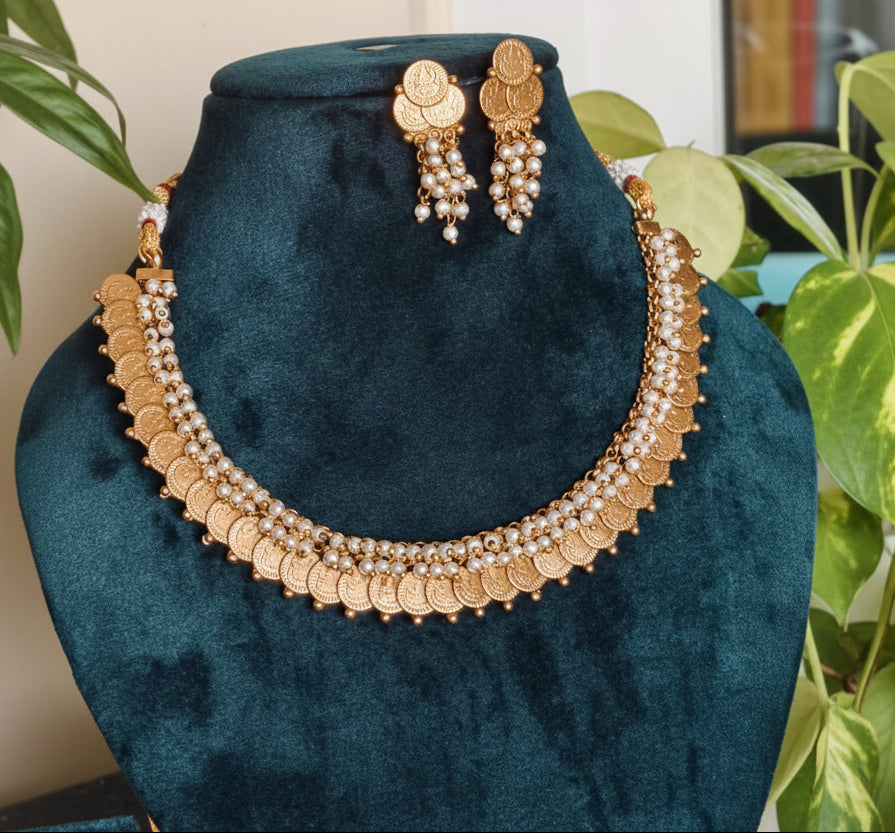 Lakshmi coin temple necklace set with pearl-like bead detailing and matching coin earrings displayed on a teal jewellery mannequin.